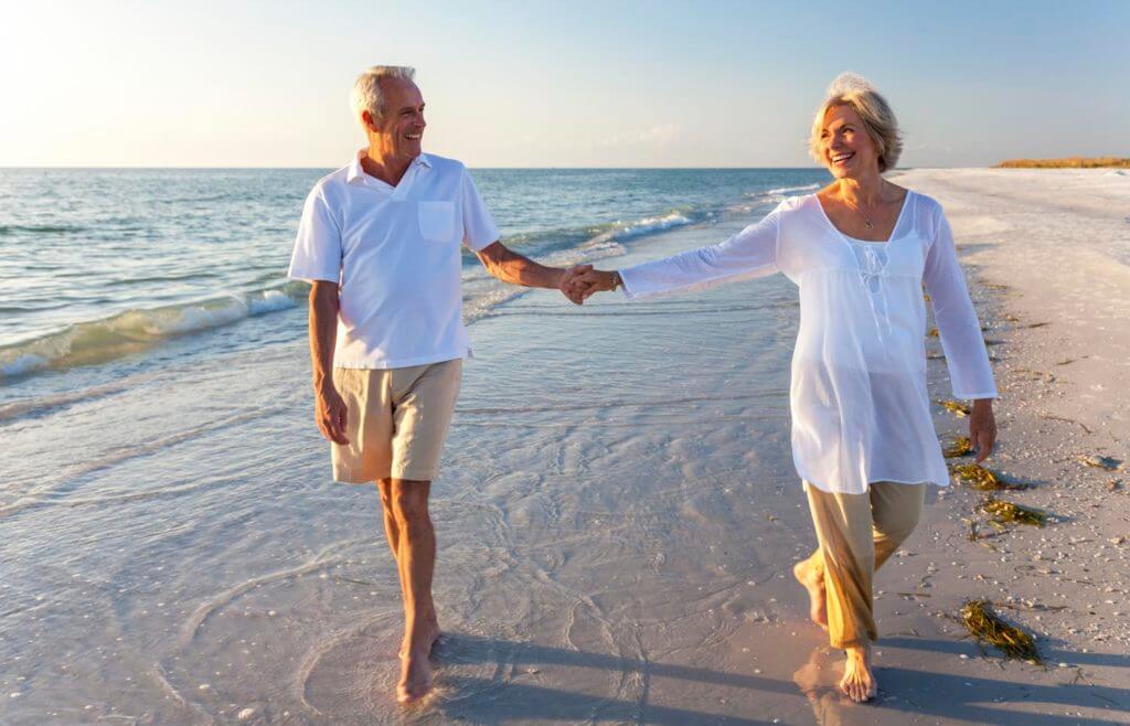 Senior couple walk near the beach shore holding hands and smiling